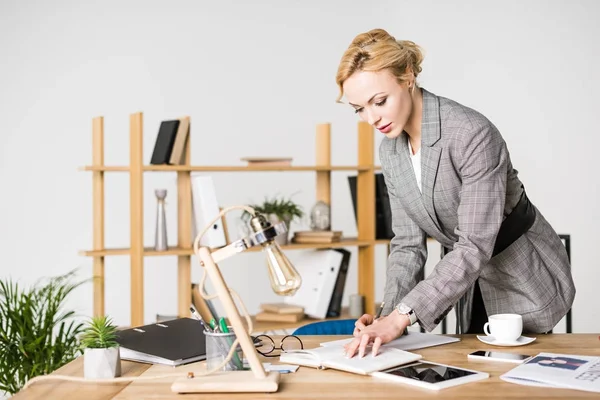 Retrato de la mujer de negocios haciendo notas en el cuaderno en el lugar de trabajo - foto de stock