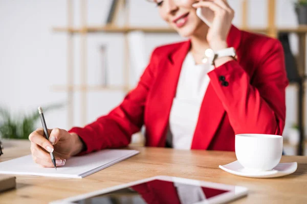 Selektiver Fokus der Geschäftsfrau, die am Arbeitsplatz im Büro mit dem Smartphone spricht — Stockfoto