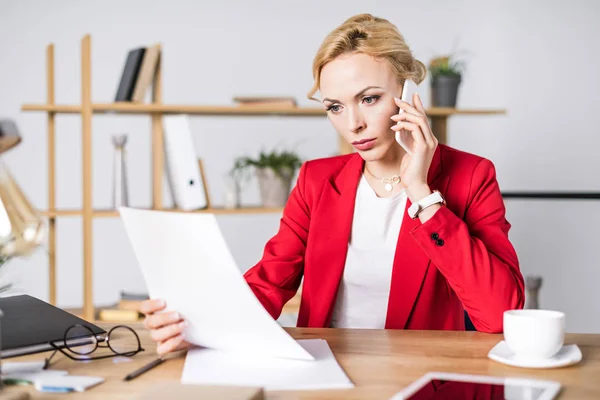 Porträt einer fokussierten Geschäftsfrau mit Dokument, die am Arbeitsplatz im Büro mit dem Smartphone spricht — Stockfoto