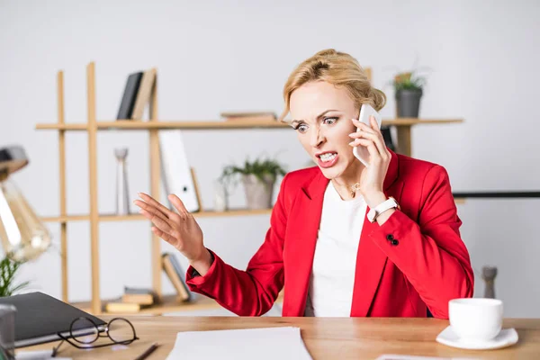 Retrato de mulher de negócios irritada falando no smartphone no local de trabalho no escritório — Fotografia de Stock