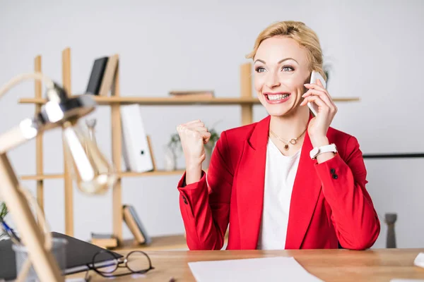 Porträt einer aufgeregten Geschäftsfrau, die am Arbeitsplatz im Büro mit dem Smartphone spricht — Stockfoto