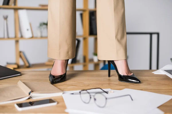 Tiro cortado de empresária de pé perto de smartphones, papéis e óculos no chão — Fotografia de Stock
