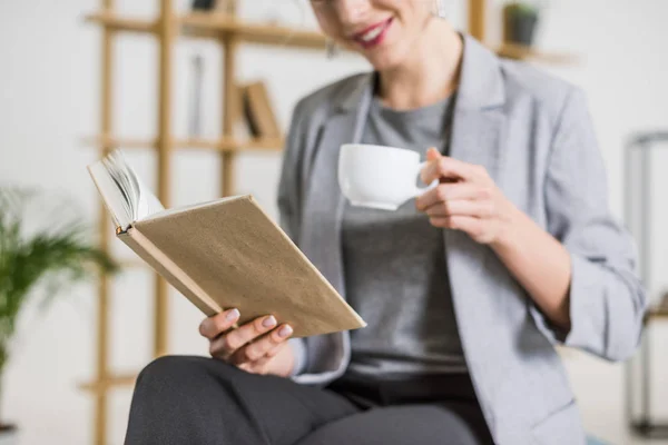 Tiro recortado de mulher de negócios sorridente com livro e xícara de café — Fotografia de Stock