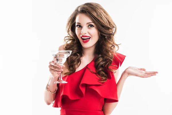Sorprendida chica de moda en vestido rojo sosteniendo vaso de cóctel aislado en blanco - foto de stock