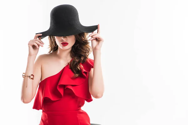 Atractiva chica de moda ocultar los ojos bajo sombrero negro aislado en blanco - foto de stock