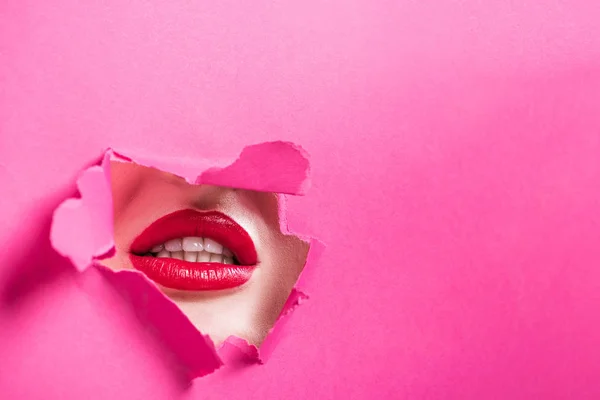 Cropped image of seductive girl showing lips in hole in pink paper — Stock Photo