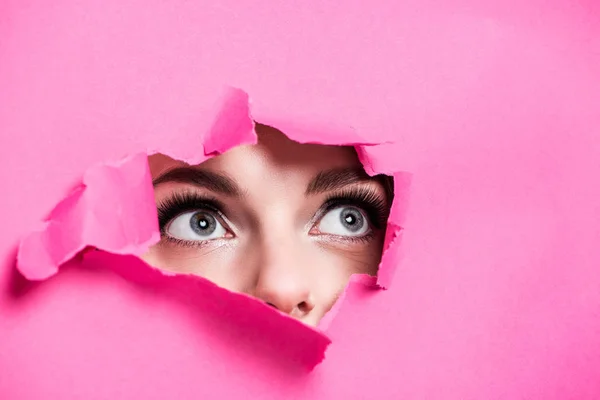 Cropped image of attractive girl looking out from hole in pink paper — Stock Photo