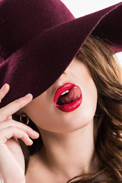 Sexy femme collant la langue dehors et cachant les yeux sous le chapeau bordeaux — Photo de stock