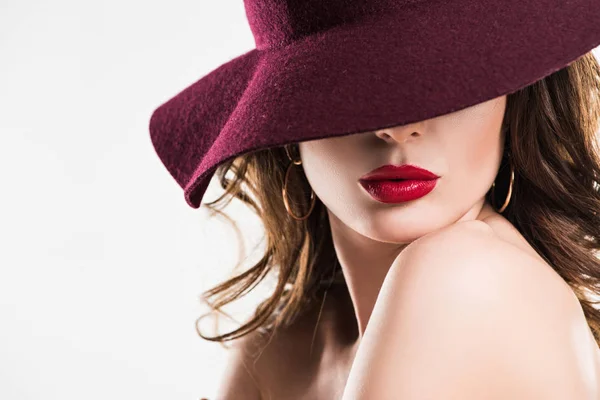 Apasionada mujer con labios rojos ocultando los ojos bajo sombrero de color burdeos aislado en blanco - foto de stock