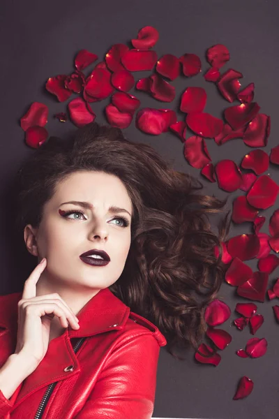 Draufsicht des nachdenklichen Mädchens, das mit Rosenblättern isoliert auf braunem, Valentinstag-Konzept liegt — Stockfoto