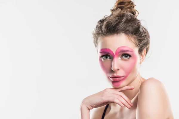 Upset girl with painted pink heart on face looking at camera isolated on white, valentines day concept — Stock Photo