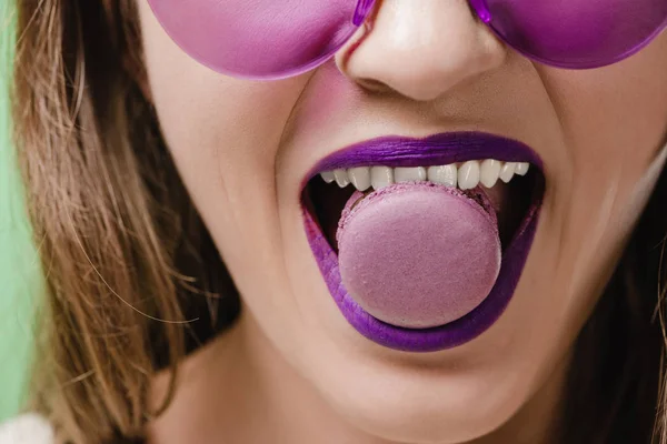 Обрезанное изображение девушки с фиолетовыми губами, кусающими макарон — стоковое фото
