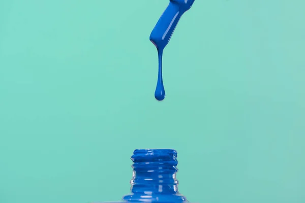 Nail polish pouring down into bottle isolated on blue — Stock Photo