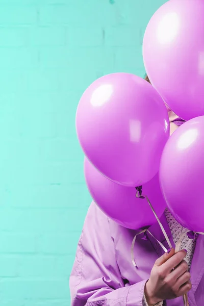 Mujer joven con abrigo escondido detrás de globos de helio rosa - foto de stock