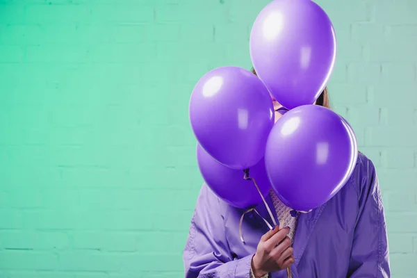 Mujer joven con abrigo escondido detrás de globos de helio púrpura - foto de stock