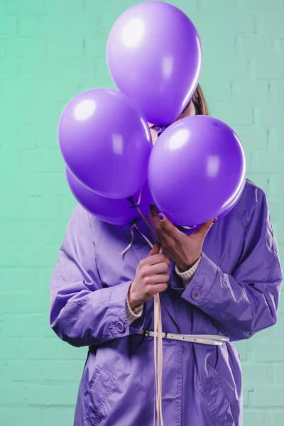 Junge Frau im Mantel versteckt sich hinter lila Luftballons — Stockfoto