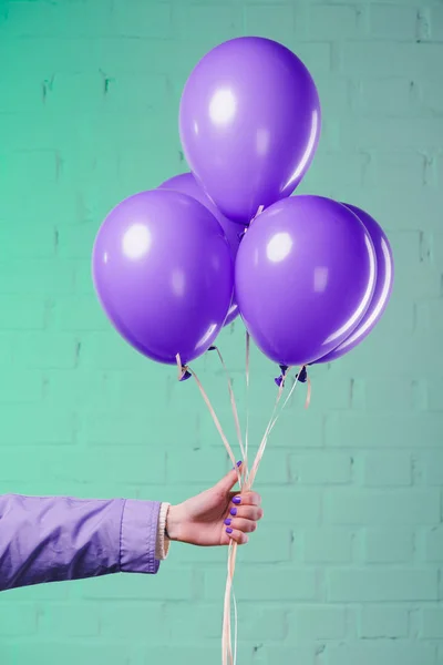 Tiro recortado de mujer sosteniendo globos de helio púrpura - foto de stock