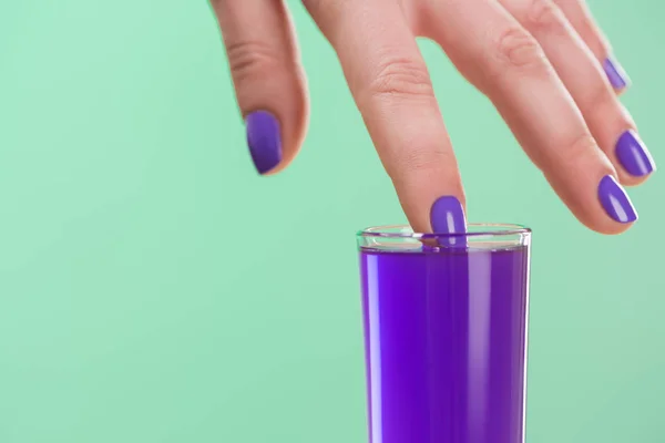 Обрезанный образ женщины, смочившей палец в фиолетовый коктейль, изолированный на бирюзовом — стоковое фото