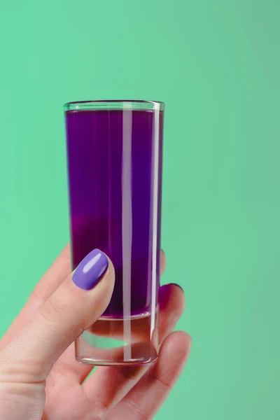 Cropped image of woman holding glass with purple cocktail isolated on turquoise — Stock Photo