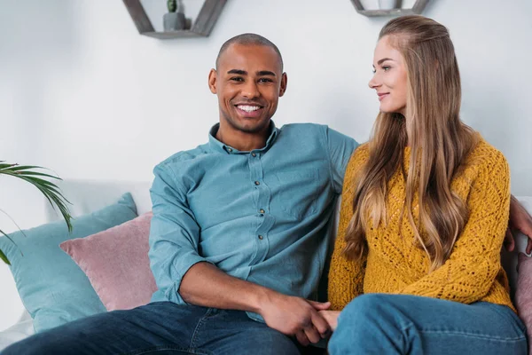 Pareja multicultural cogida de la mano en el sofá - foto de stock