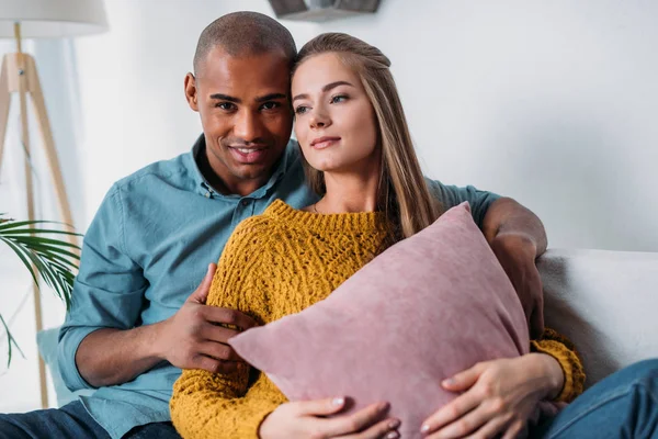 Cariñosa pareja multicultural abrazándose en el sofá - foto de stock