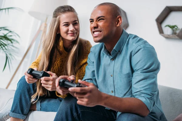 Улыбающаяся мультикультурная пара, играющая в видеоигры дома — стоковое фото