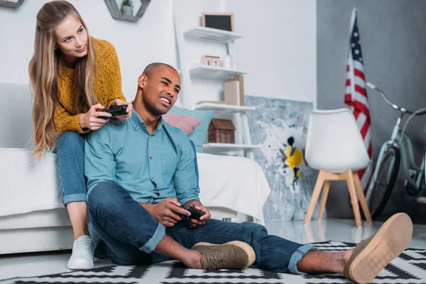 Pareja multicultural jugando videojuego en casa - foto de stock