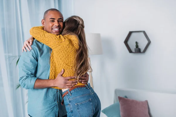 Lächelndes multikulturelles Paar umarmt sich im Zimmer — Stockfoto