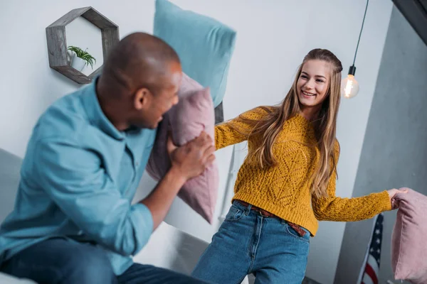 Multicultural couple having fun and fighting with pillows — Stock Photo