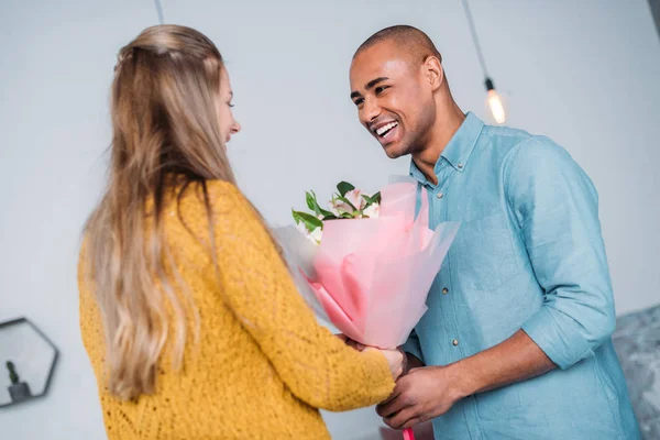 Sonriente afroamericano novio presentando ramo a novia - foto de stock