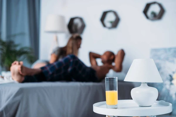 Мультикультурная пара лежит на кровати с апельсиновым соком на переднем плане — стоковое фото