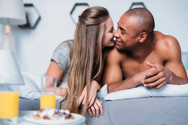 Многокультурная пара целуется и лежит на кровати — стоковое фото
