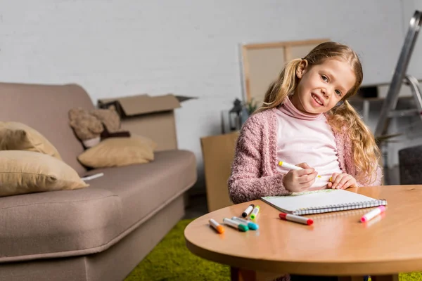 Cute little child drawing with felt tip pens and smiling at camera at home — Stock Photo