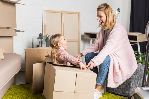 Happy mother and daughter looking at each other while playing with cardboard boxes during relocation — Stock Photo