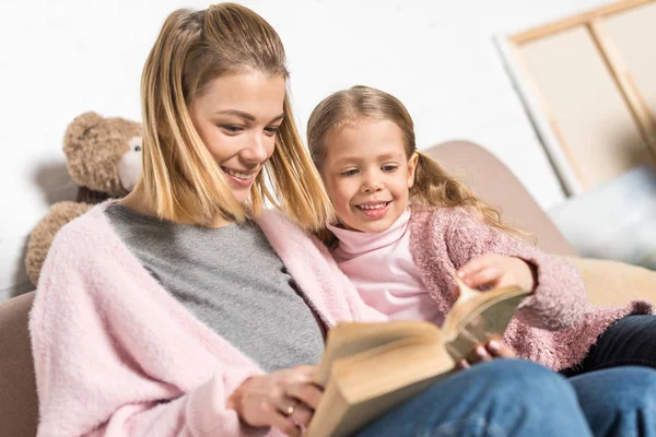 Mãe feliz e filha lendo livro juntos no sofá — Fotografia de Stock