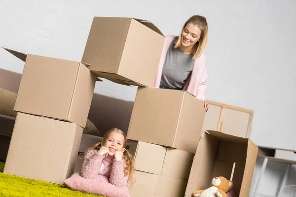 Madre e hija se divierten con cajas de cartón mientras se mudan a casa - foto de stock