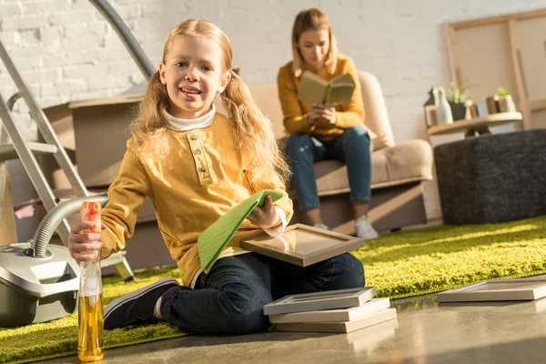 Carino poco bambino pulizia cornici e sorridente a macchina fotografica mentre la madre lettura libro dopo il trasferimento — Foto stock