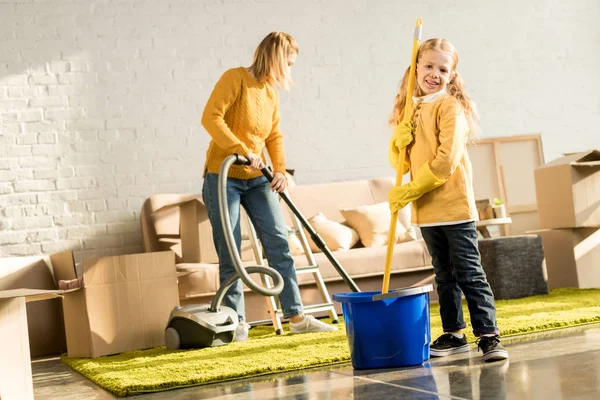 Mãe e filha com esfregona e aspirador de pó sala de limpeza após a realocação — Fotografia de Stock