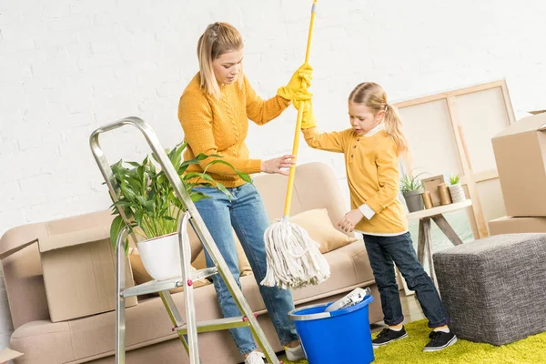 Mother and daughter holding mop and cleaning room after relocation — Stock Photo