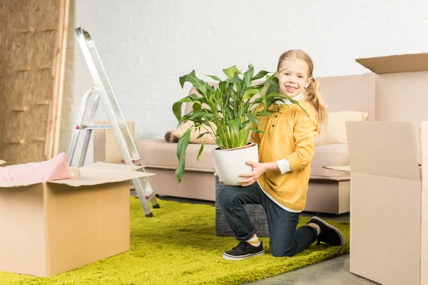 Glückliches kleines Kind hält Zimmerpflanze in der Hand und lächelt in die Kamera, während es nach Hause zieht — Stockfoto