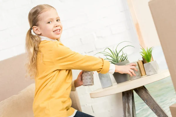 Niedliches kleines Kind lächelt in die Kamera, während es beim Umzug Kerzen auf den Tisch stellt — Stockfoto