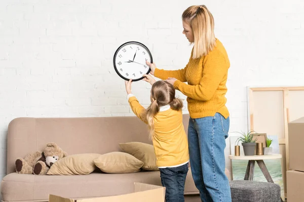 Красивая мать и дочь висят часы на стене во время переезда — стоковое фото