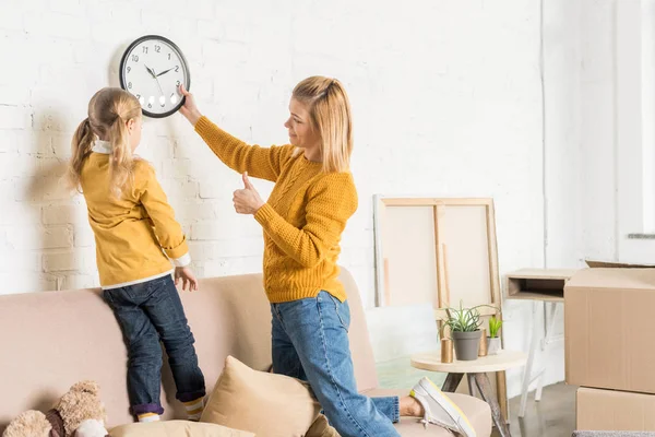 Mother and daughter hanging clock on wall during relocation — Stock Photo