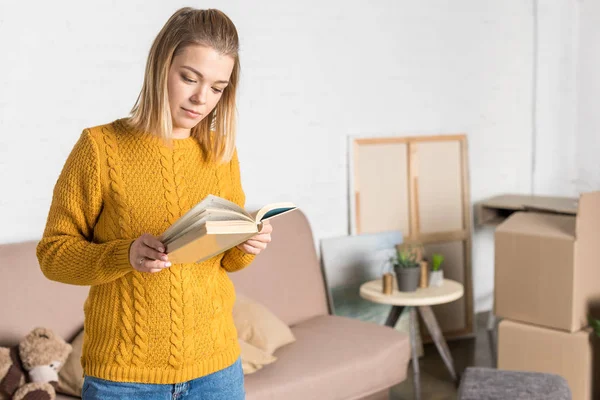 Attractive young woman reading book while moving home — Stock Photo