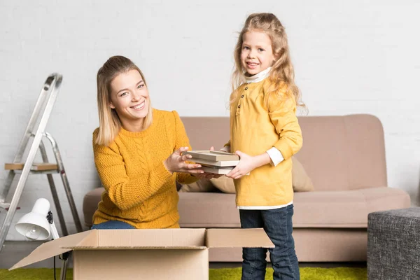 Happy mother and daughter holding books and smiling at camera while relocating — Stock Photo