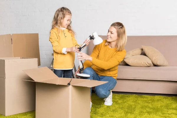 Mãe feliz e filha segurando lâmpada ao se mudar para casa — Fotografia de Stock