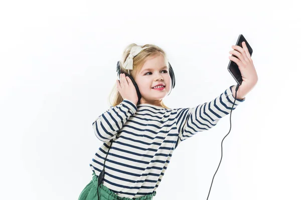 Adorable niño pequeño con auriculares tomando selfie aislado en blanco - foto de stock