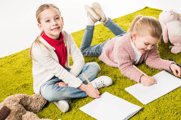 Schöne kleine Schwestern, die auf dem Fußboden vereint auf weiß zeichnen — Stockfoto