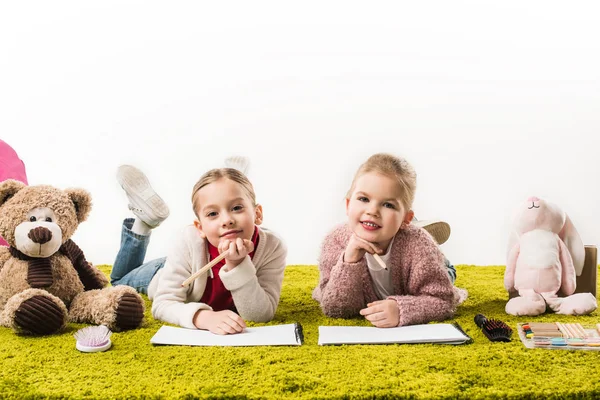 Adorables hermanas pequeñas dibujando con lápices de color juntos en el suelo aislado en blanco - foto de stock