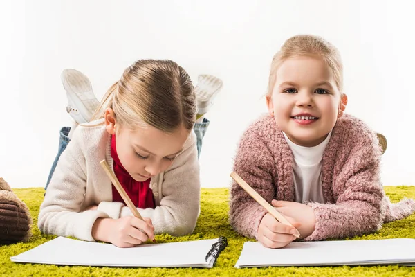 Hermanas pequeñas felices dibujando con lápices de color juntos en el suelo aislado en blanco - foto de stock